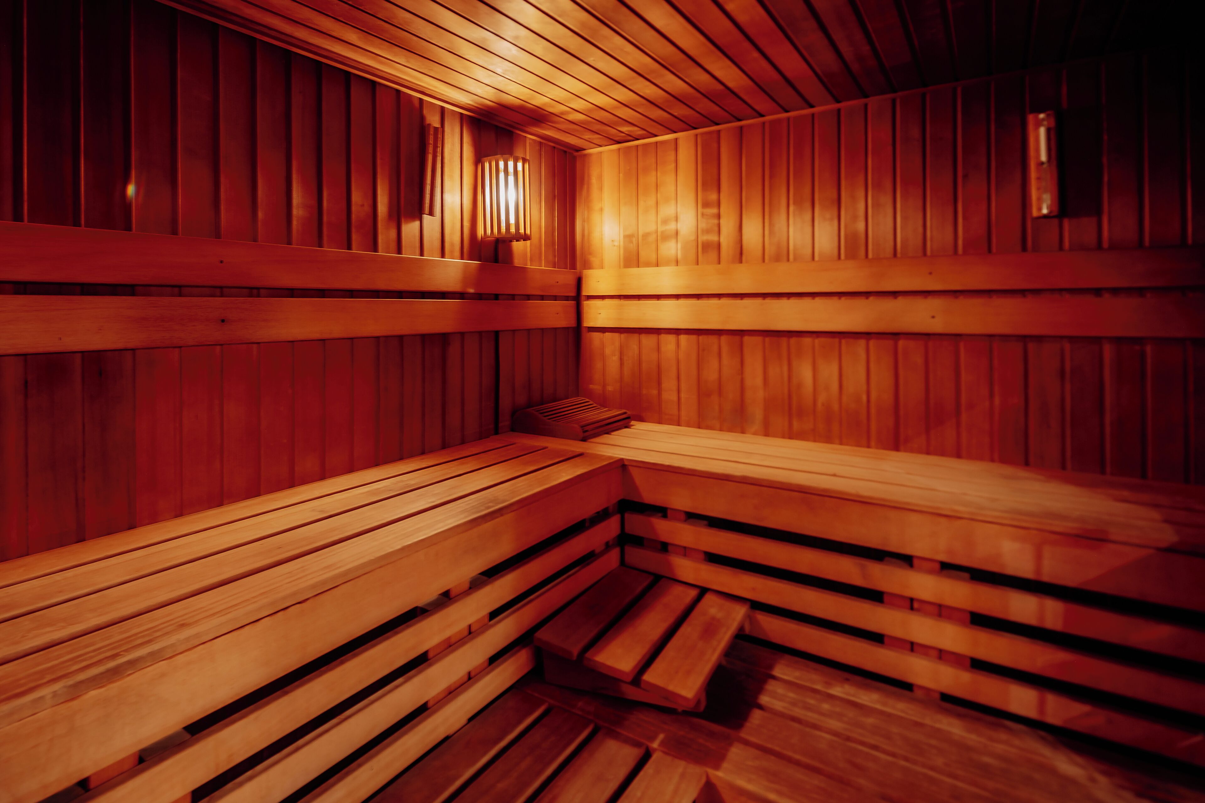 Una sauna con bancos y paredes de madera, un calentador para los bancos y una luz instalada en la pared.