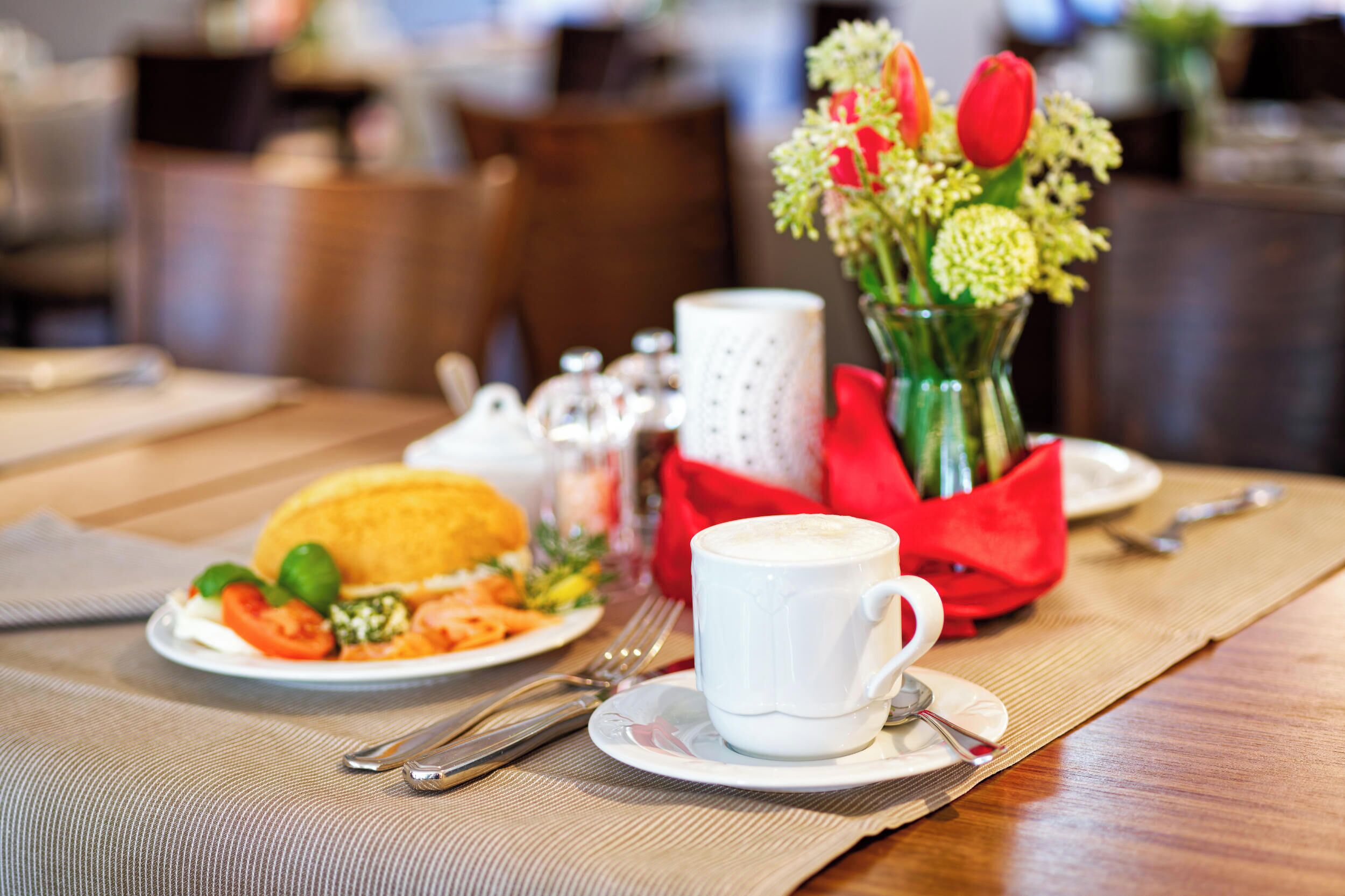 A breakfast setting with a plate of food, a cup of coffee, and a vase of flowers on a table.