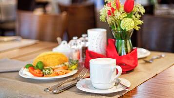 A breakfast setting with a plate of food, a cup of coffee, and a vase of flowers on a table.
