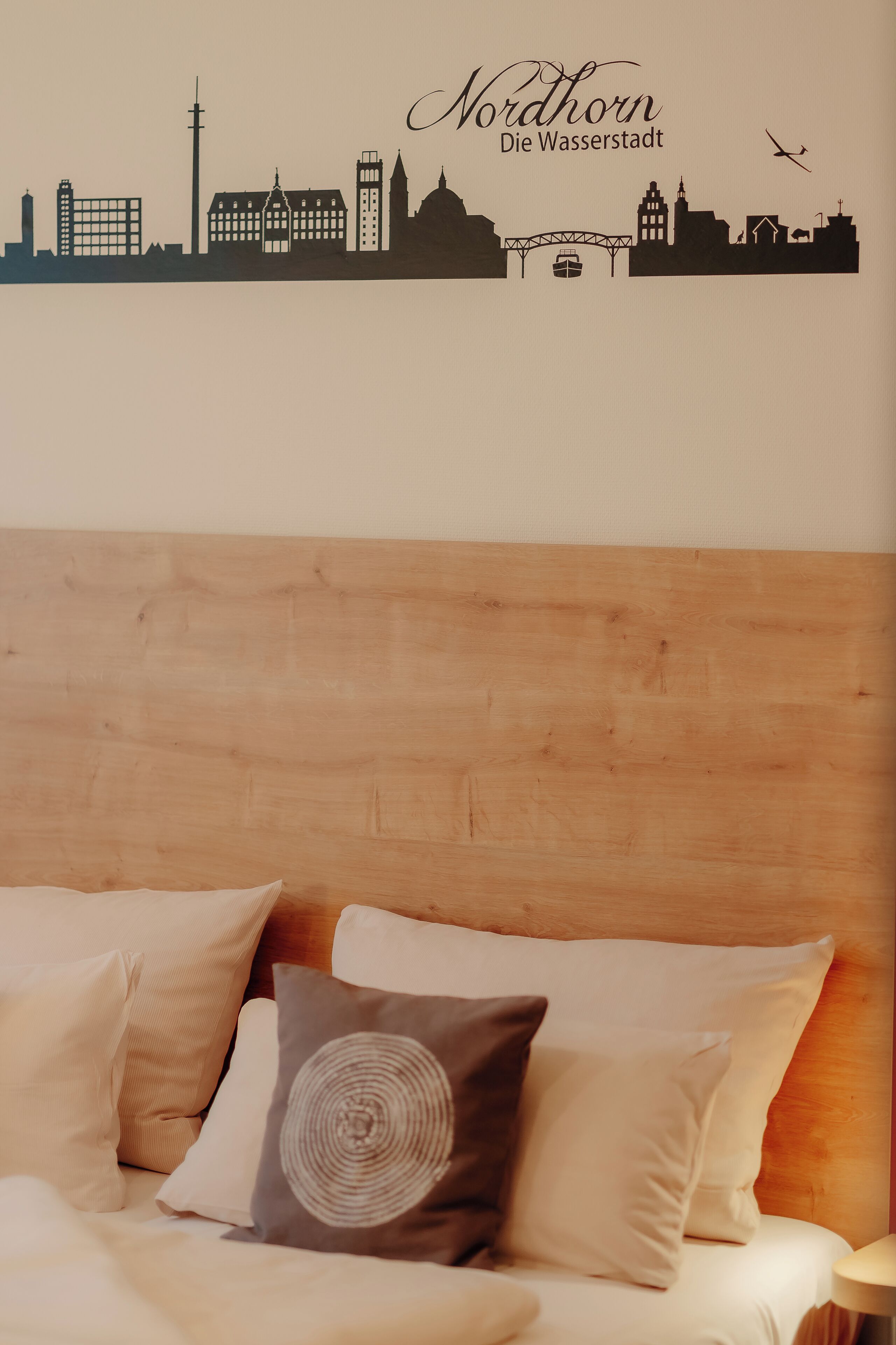 A bed with a city skyline wall art, pillows, and a wooden headboard.