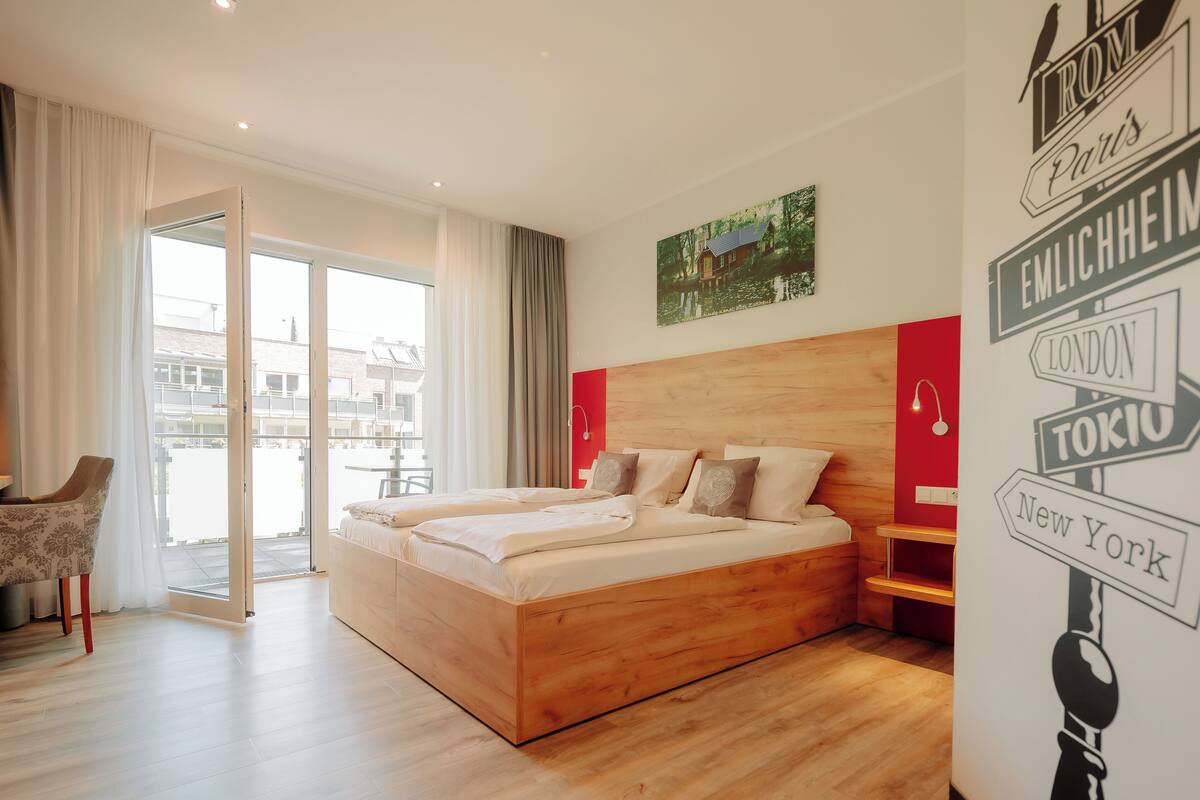 Quarto de hotel moderno com uma cama grande, uma cadeira e vista para o exterior.
