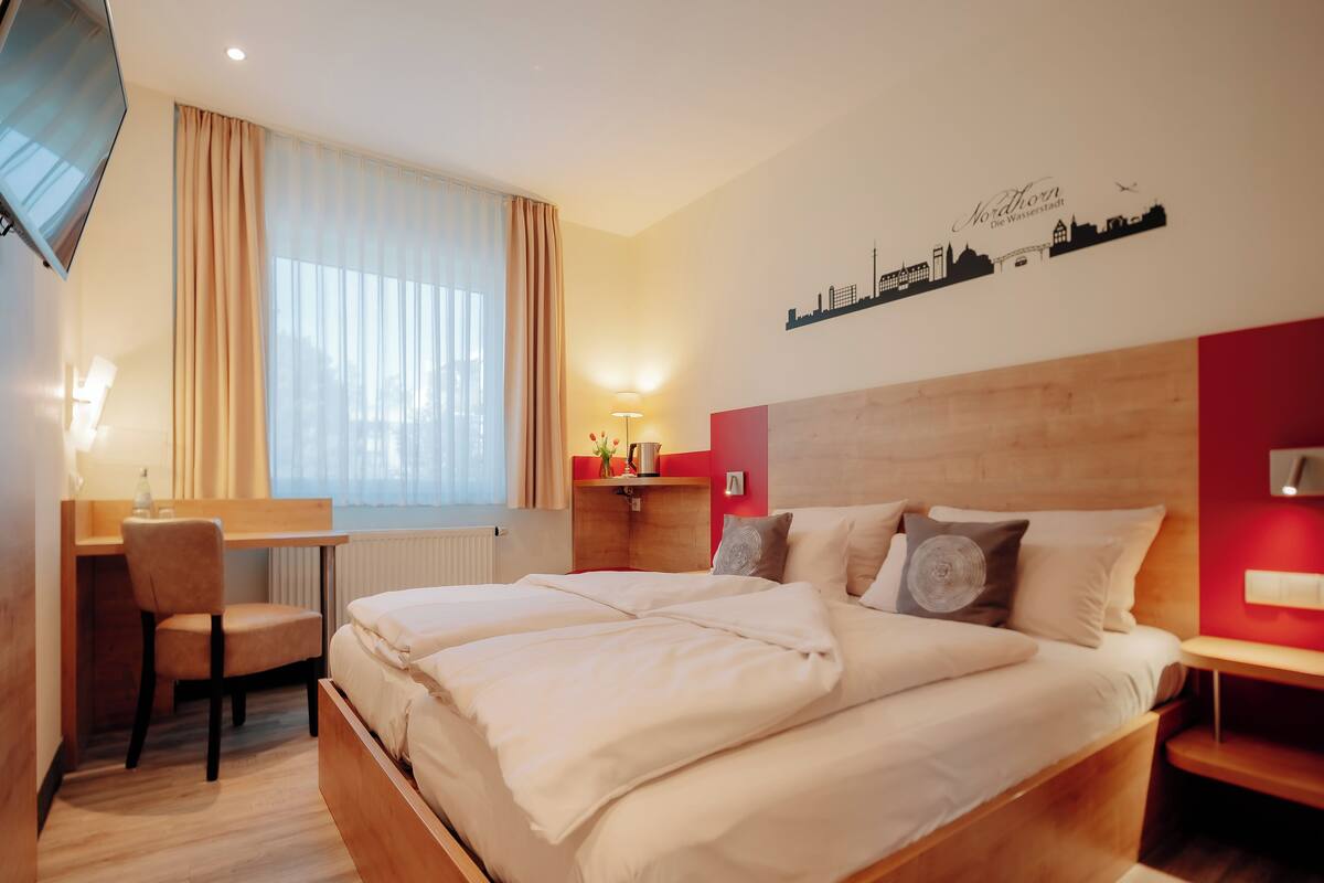 Quarto de hotel com cama, escrivaninha, cadeira e decoração de parede com vista urbana.