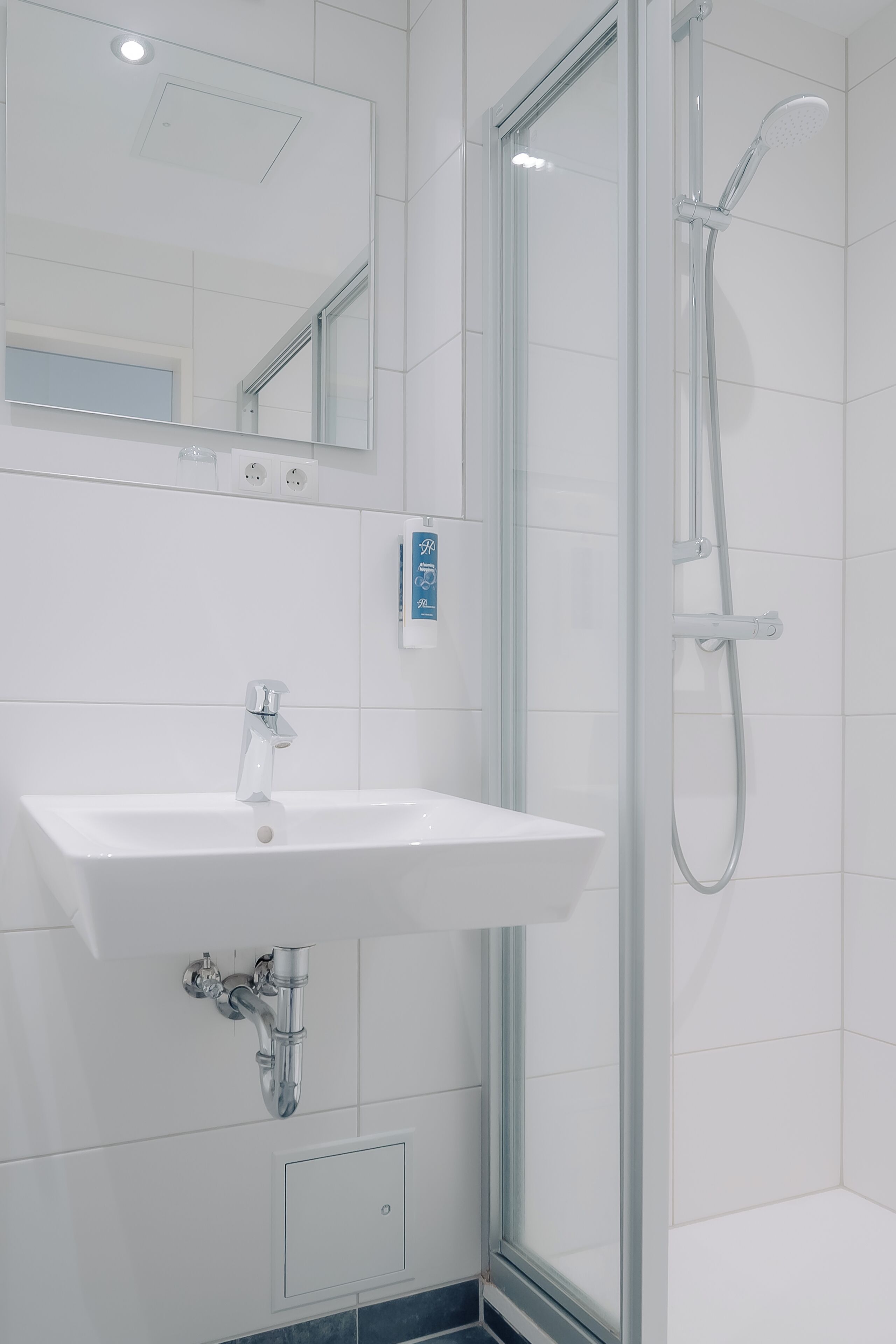A modern bathroom with a white sink, a mirror, and a glass-enclosed shower.