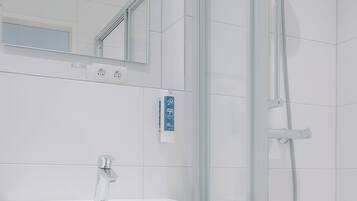 A modern bathroom with a white sink, a mirror, and a glass-enclosed shower.