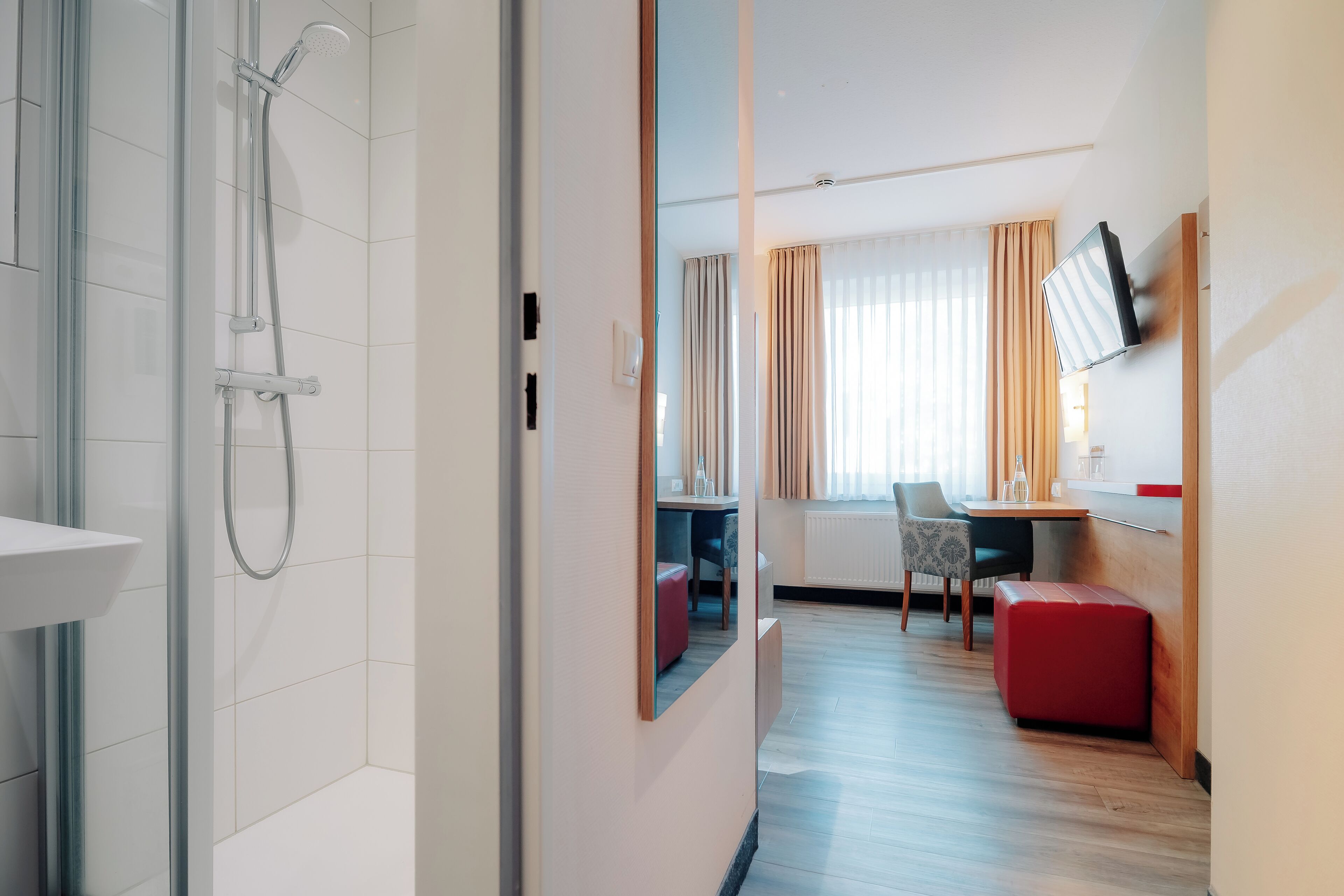 Una habitación de hotel moderna con ducha, un área de comedor con mesa y sillas, y un televisor montado en la pared.