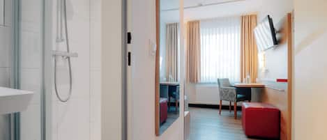 Una habitación de hotel moderna con ducha, un área de comedor con mesa y sillas, y un televisor montado en la pared.