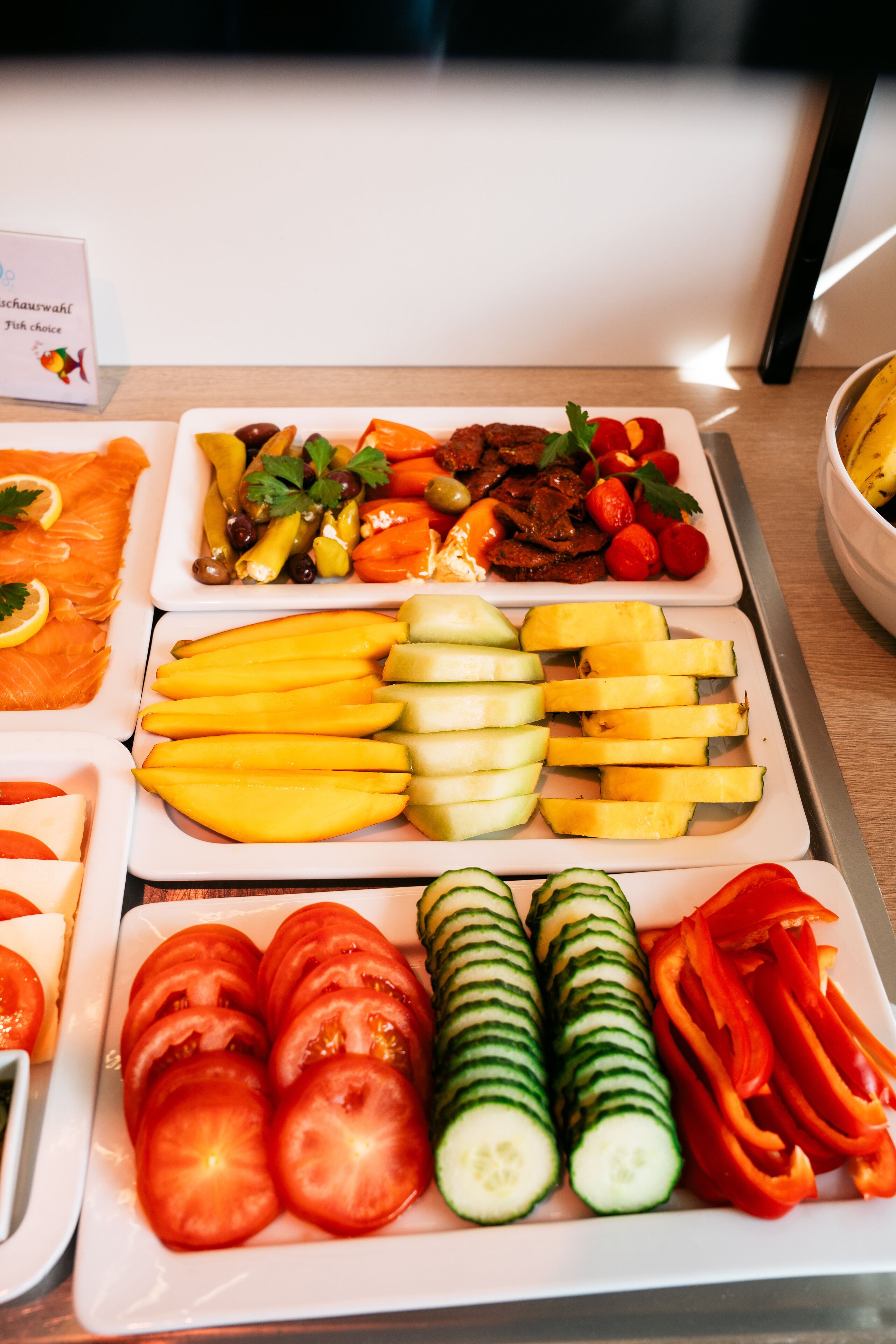 Un bufé con diversas opciones de comida, incluyendo salmón, frutas, verduras y un cartel que indica la selección de pescado.