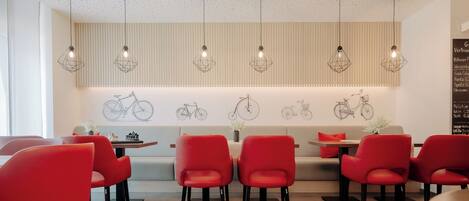 Un comedor moderno con sillas rojas, una mesa de madera y lámparas colgantes.