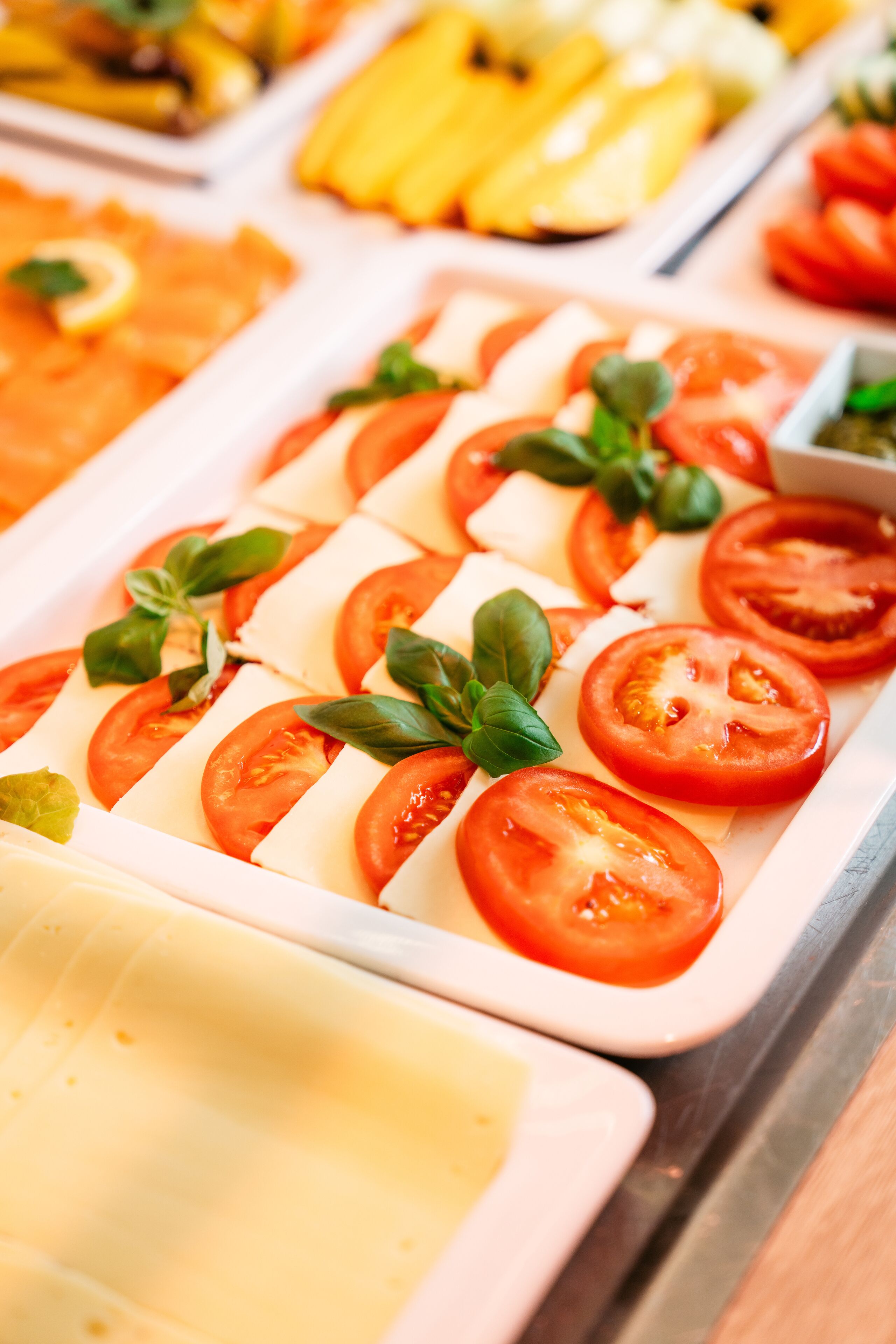 Un bufé con diversas opciones de comida, entre ellas tomates en rodajas y queso.
