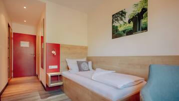 A hotel room with a wooden bed, a red wall, a small bedside table, and a picture of a tree.
