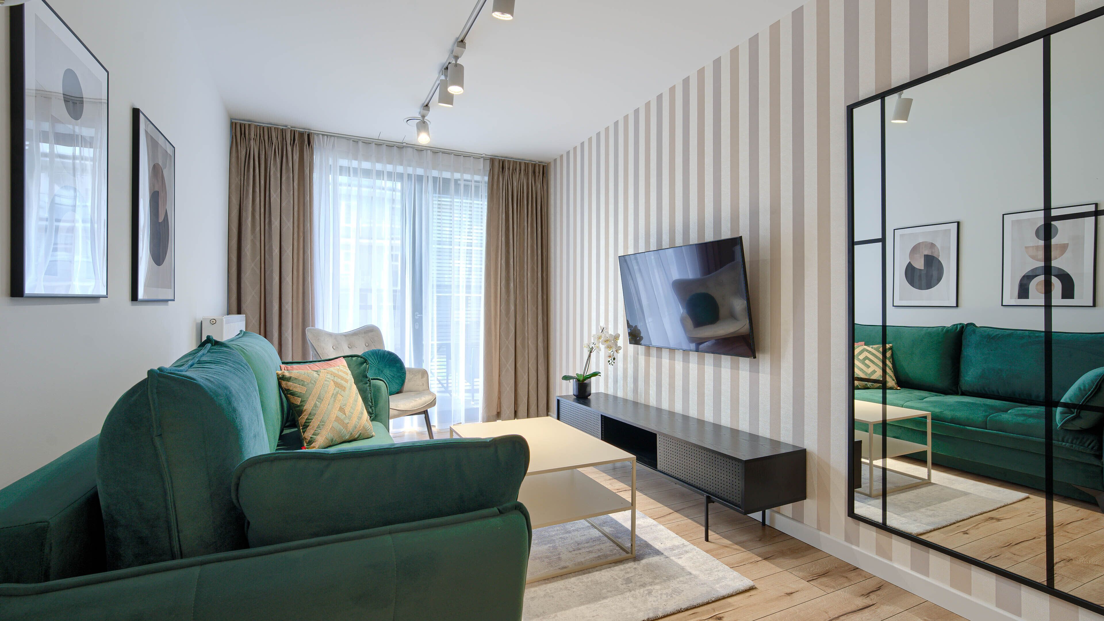 Een moderne woonkamer met een groene bank, een salontafel en een aan de muur bevestigde televisie.