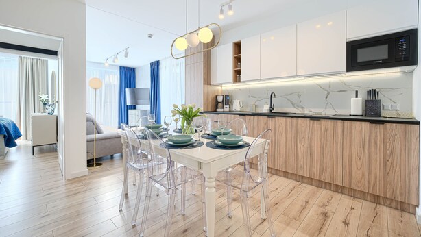 A modern kitchen with a microwave, wooden cabinets, and a dining area with a white table and clear chairs.