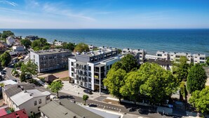 A modern building complex with multiple floors, surrounded by trees and a view of the sea.