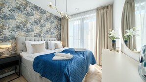 A modern bedroom with a large bed, a textured wall, a chandelier, and a view of the outdoors.