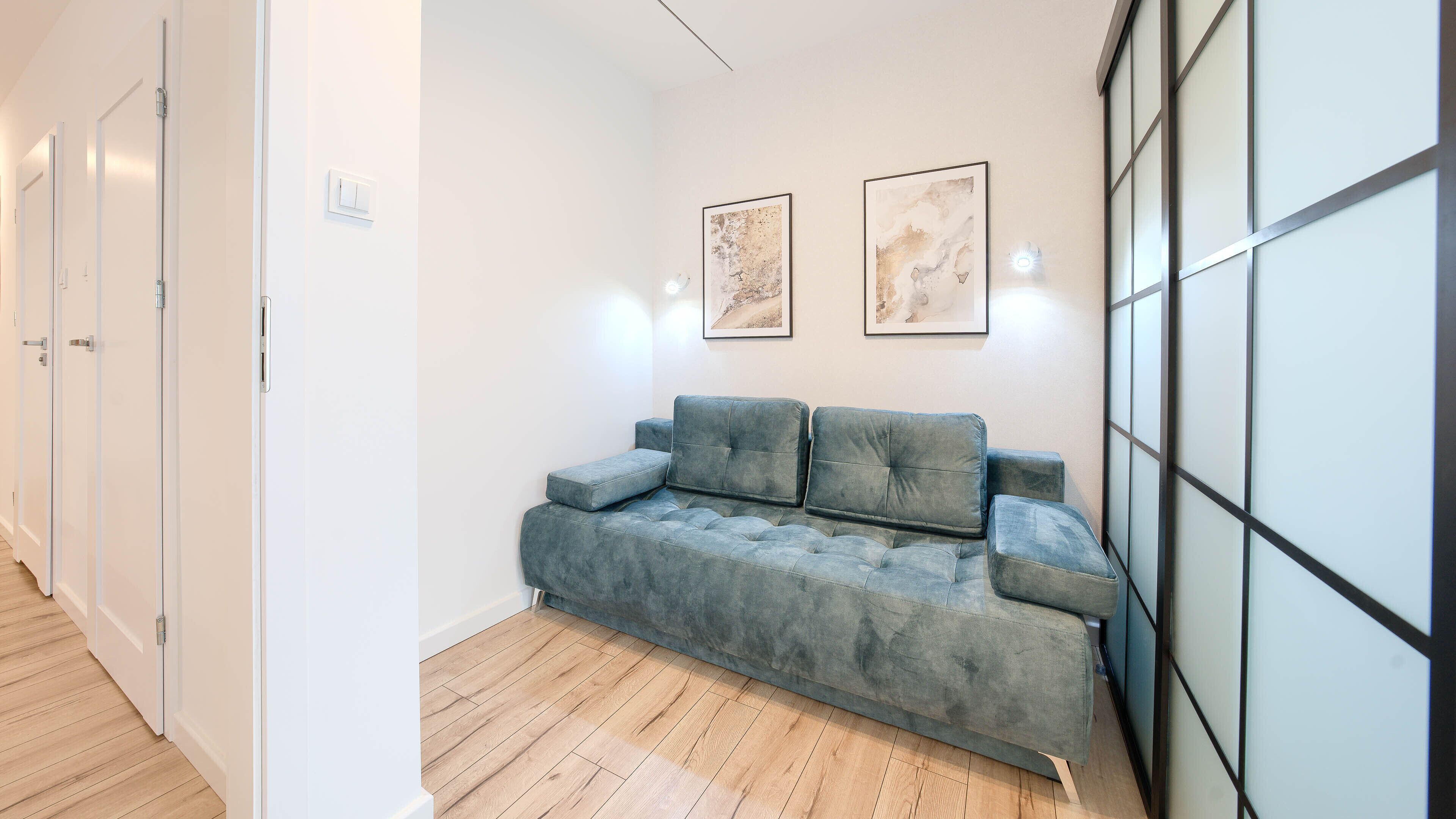 A modern interior with a grey sofa, wooden flooring, and two abstract paintings on the wall.