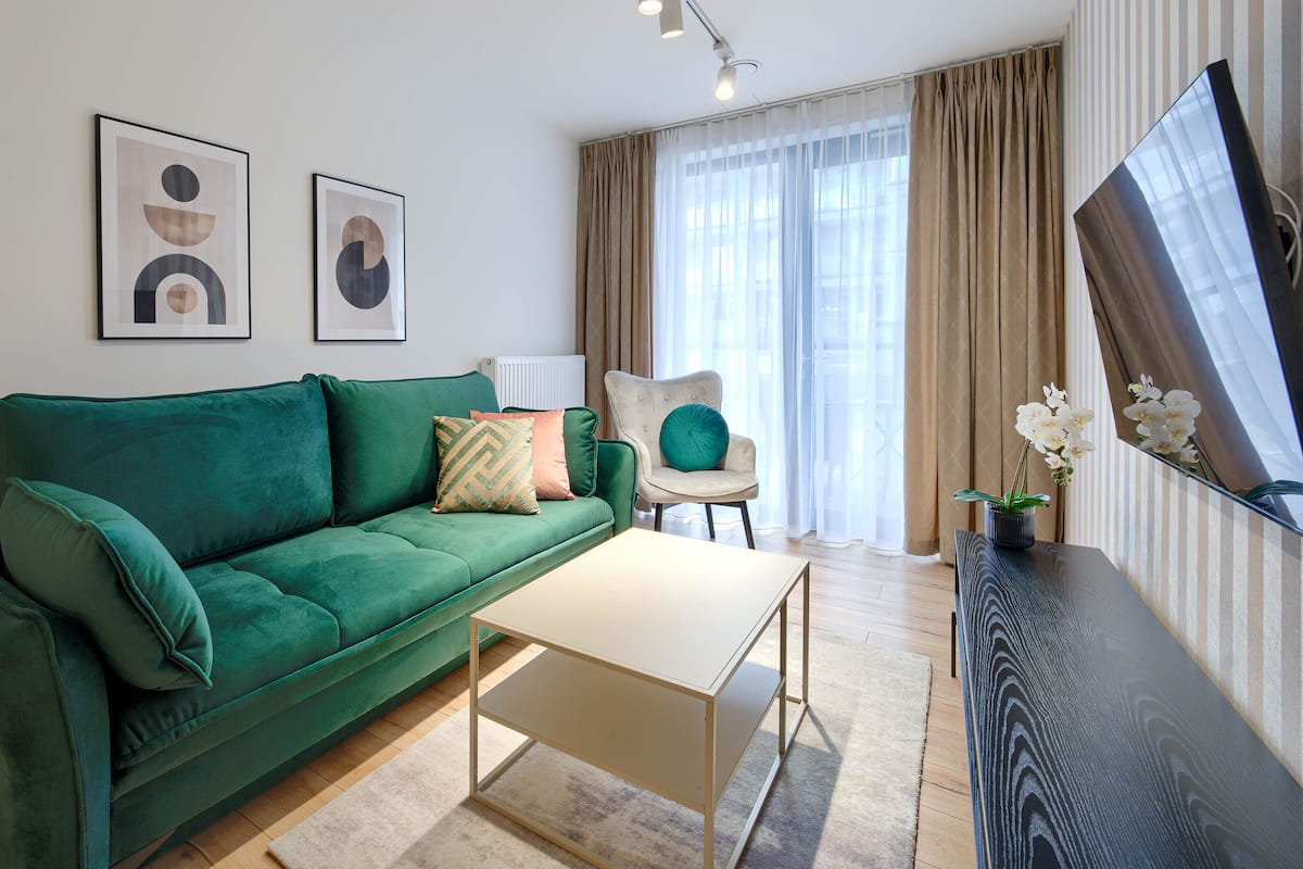 Ein modernes Wohnzimmer mit einem grünen Sofa, einem Couchtisch, einem Fernseher und einem Fenster mit Vorhängen.