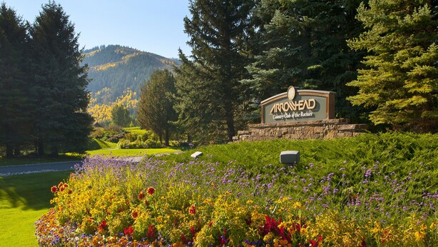 Skilt for Arrowhead Country Club of the Rockies omgivet af en blomsterfuld have.