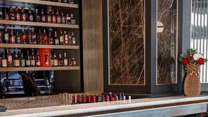 Un espace bar doté d’un comptoir en marbre, de plusieurs étagères remplies de bouteilles d’alcool et de tabourets de bar noirs.