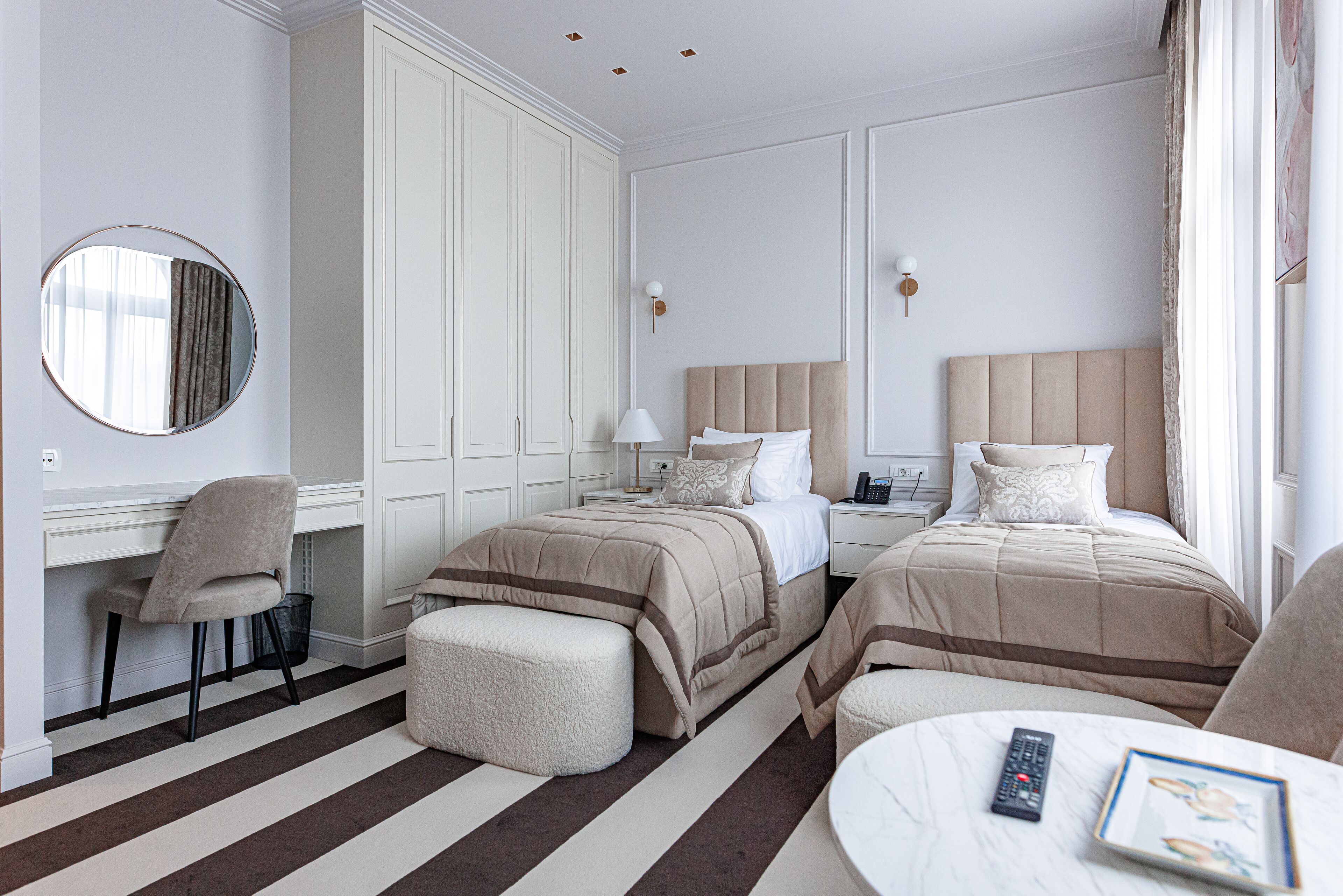 A hotel room with two beds, a desk, a chair, a round table, and a large mirror.
