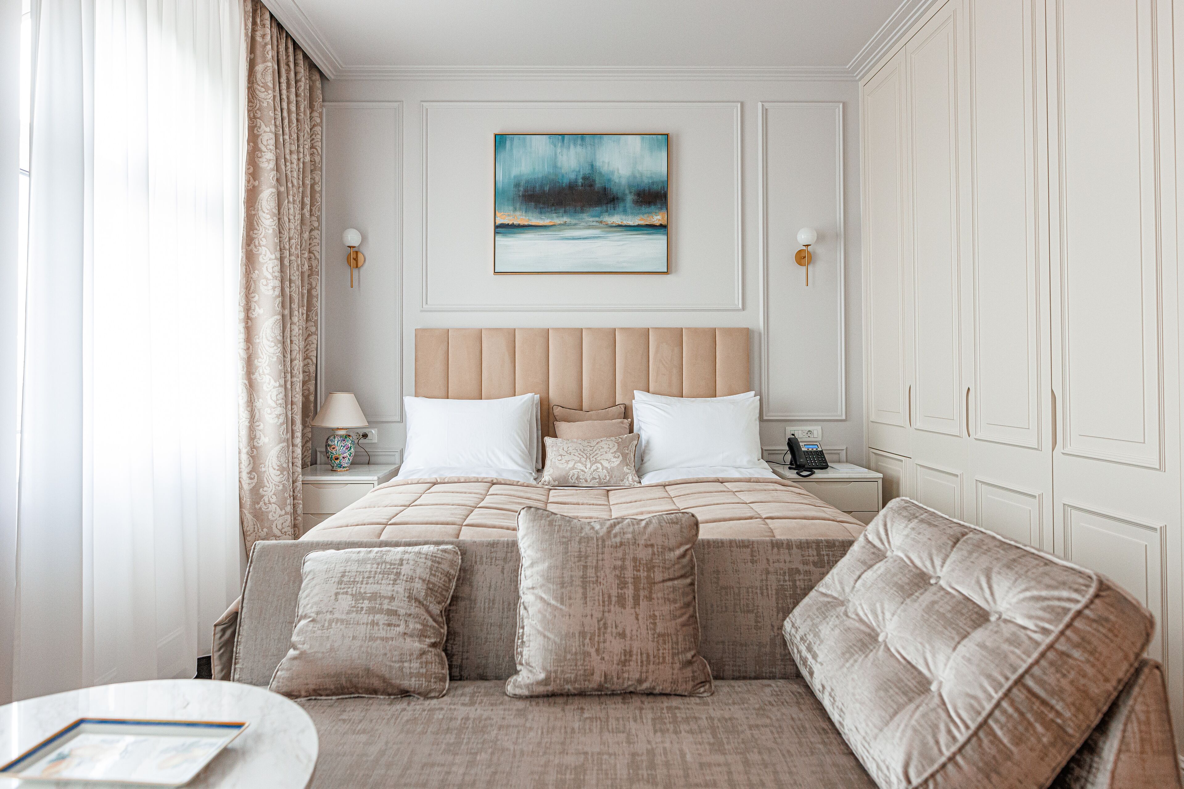 Habitación de hotel con una cama grande, una mesita de noche con lámpara, un cuadro en la pared y un sofá con cojines.