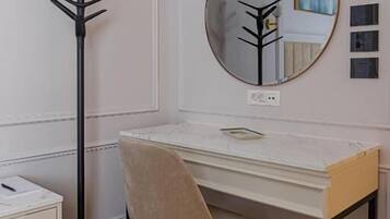 A white desk with a round mirror, a beige chair, and a black coat rack.