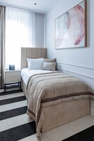 Un dormitorio ordenado con cama, mesita de noche y un cuadro abstracto grande en la pared.