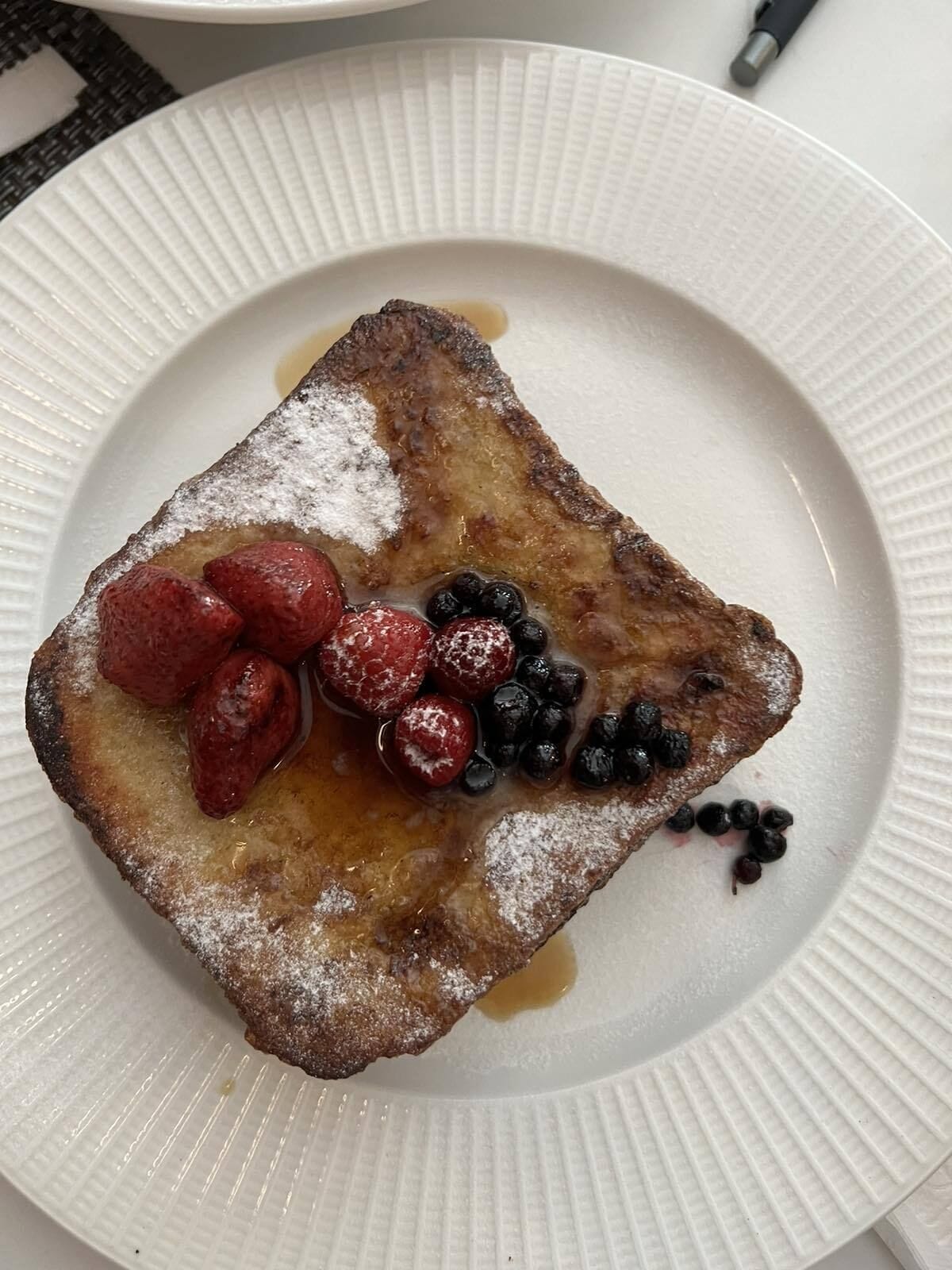 Un plato con tostadas francesas, fresas, arándanos y jarabe.