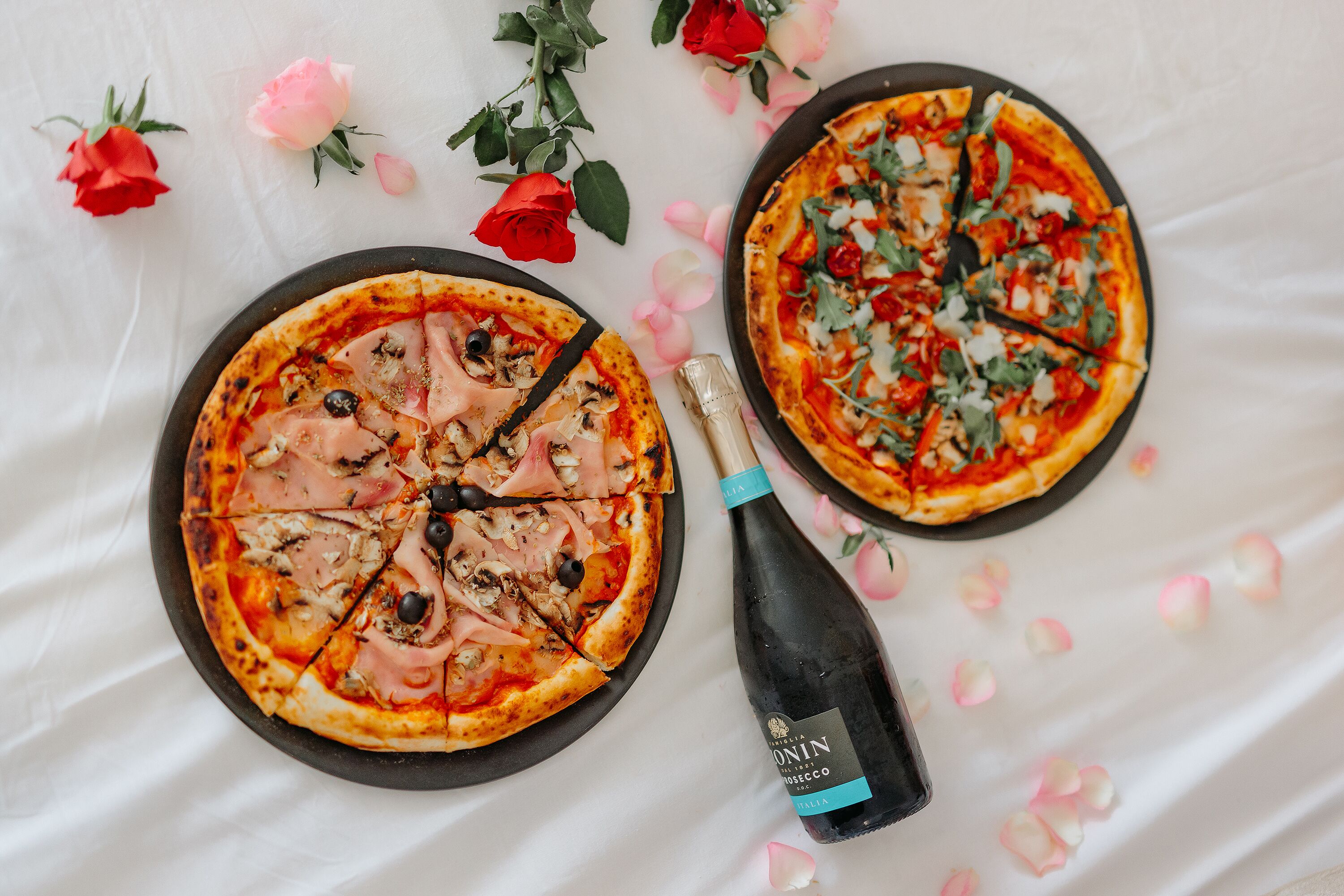 Two pizzas on plates with rose petals scattered around.