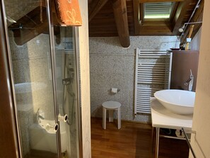 Une salle de bain avec une douche à parois de verre, un lavabo blanc, un petit tabouret et un porte-serviettes.