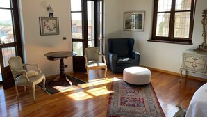A room with hardwood flooring, a round table, two chairs, a blue armchair, a white ottoman, and a patterned rug.