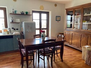 Un coin repas avec une table et des chaises en bois, un réfrigérateur, une fenêtre avec vue et un meuble avec des portes en verre.