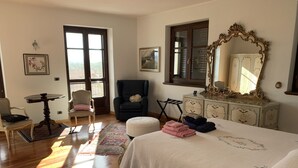 A bedroom with a large bed, a dresser, a chair, a table, and a window with a view.