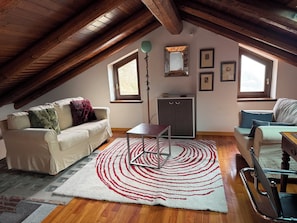 Une pièce mansardée avec un plafond haut, des poutres en bois, un canapé, une petite table, une armoire et un miroir.