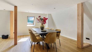 Ein Essbereich mit einem Holztisch und Stühlen, einer Vase mit Blumen und einem Fenster mit Blick.