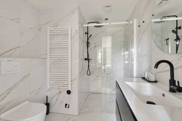 Un baño moderno con ducha de vidrio, lavamanos blanco y un inodoro.