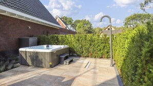 Ein Whirlpool in einem Garten mit einer Backsteinmauer, einem Metalldach und einer Hecke.