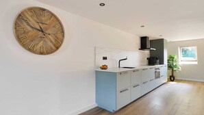 Eine moderne Küche mit einer großen Holz-Standuhr, hellblauen Schränken und einem Fenster, das natürliches Licht hereinlässt.
