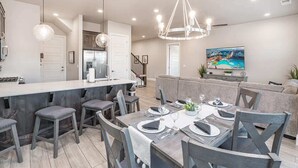 Une cuisine moderne dotée d’un îlot central, de tabourets de bar et d’un coin repas avec une table dressée pour quatre personnes.