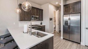 Une cuisine moderne avec des meubles en bois foncé, des appareils électroménagers en acier inoxydable et des luminaires suspendus.