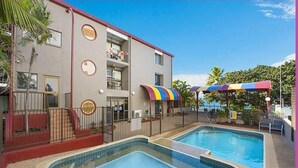 Un hotel con piscina, mobiliario exterior y una zona cubierta con sombrillas de colores.
