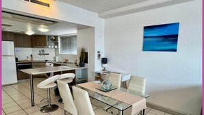 Una cocina moderna con comedor, que incluye una mesa de vidrio y taburetes de bar, un cuadro en la pared y vistas al mar.