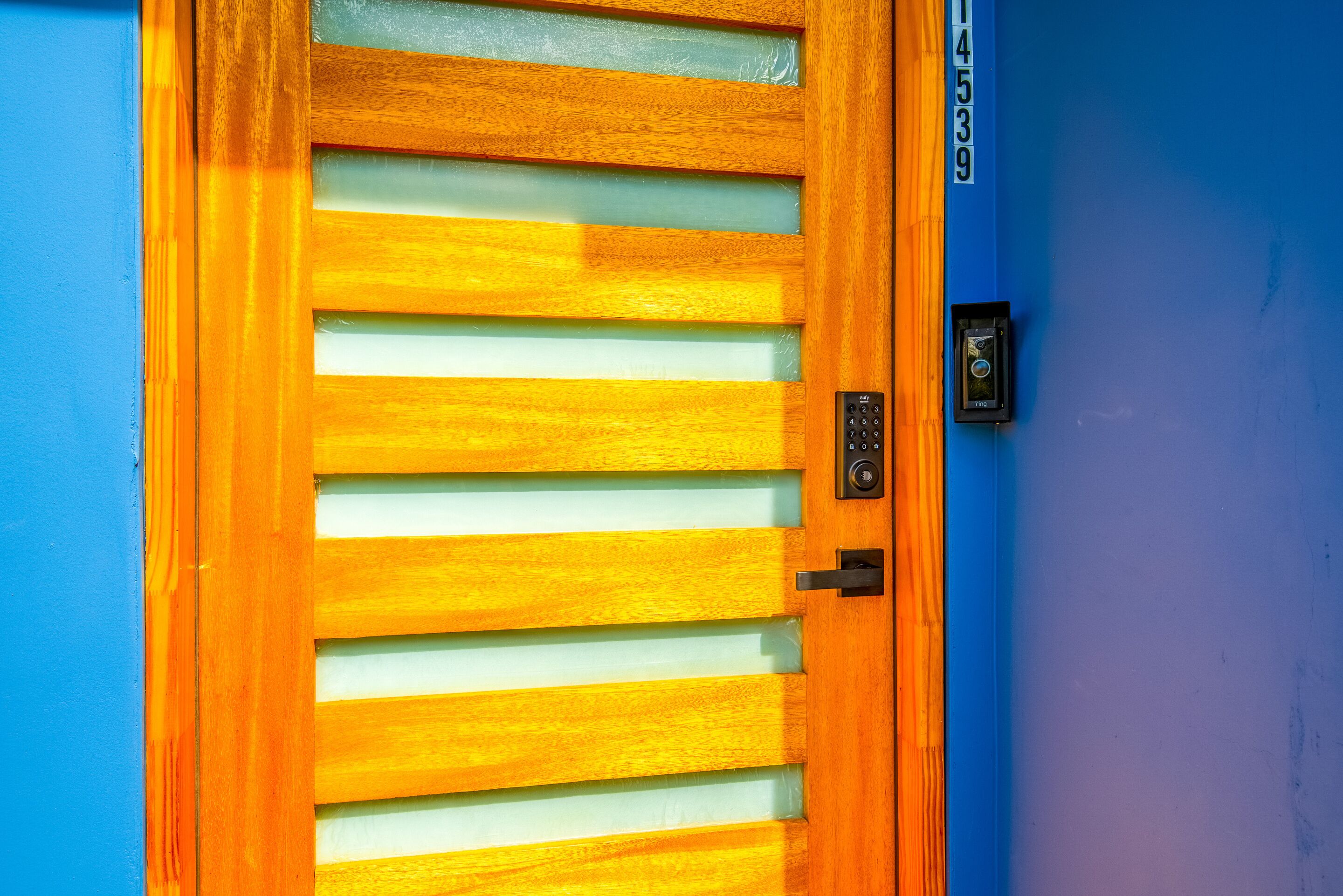 A wooden door with horizontal slats, a keypad lock, and a number plate on a blue wall.