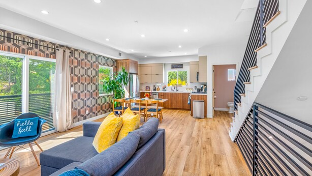 A modern living room with a sofa, a dining table, and a kitchen in the background. - Stylish Sherman Oaks Townhouse W/ 3 Master Suites (Van Nuys)