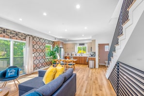 Uma sala de estar moderna com um sofá, uma mesa de jantar e uma cozinha ao fundo.