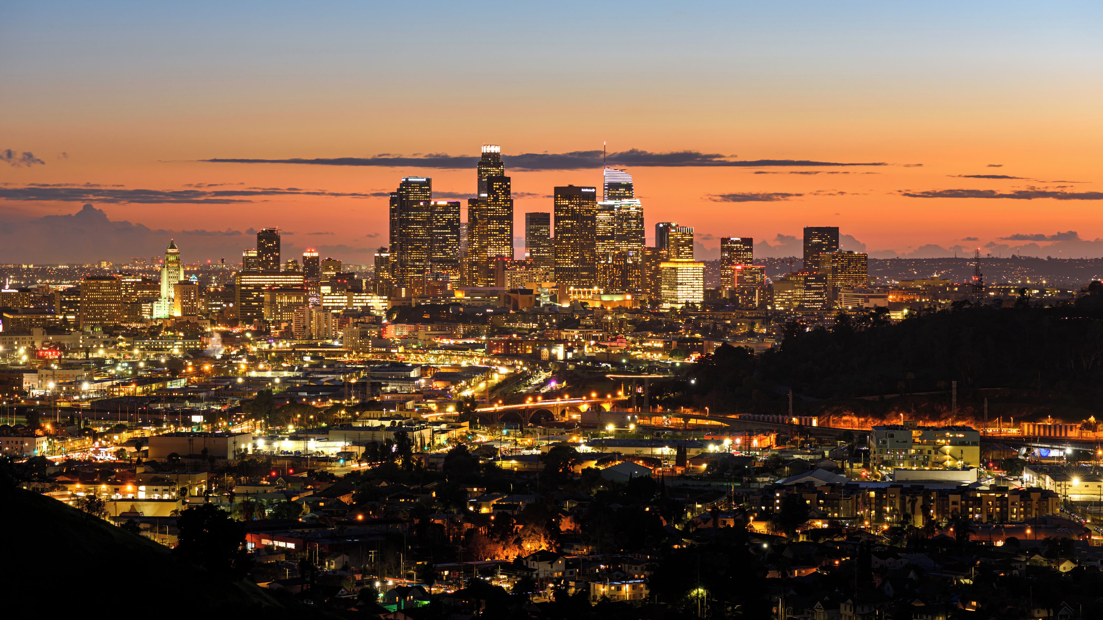 A city skyline at dusk with illuminated buildings and a bridge.