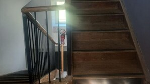 Eine Holztreppe mit Metallgeländer, die zu einer Zwischenebene mit einem Feuerlöscher führt.