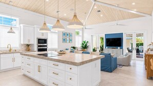 A modern kitchen with white cabinetry, gold handles, and pendant lighting.