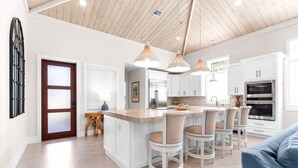A modern kitchen with white cabinets, a central island, bar stools, pendant lighting, and a large window.