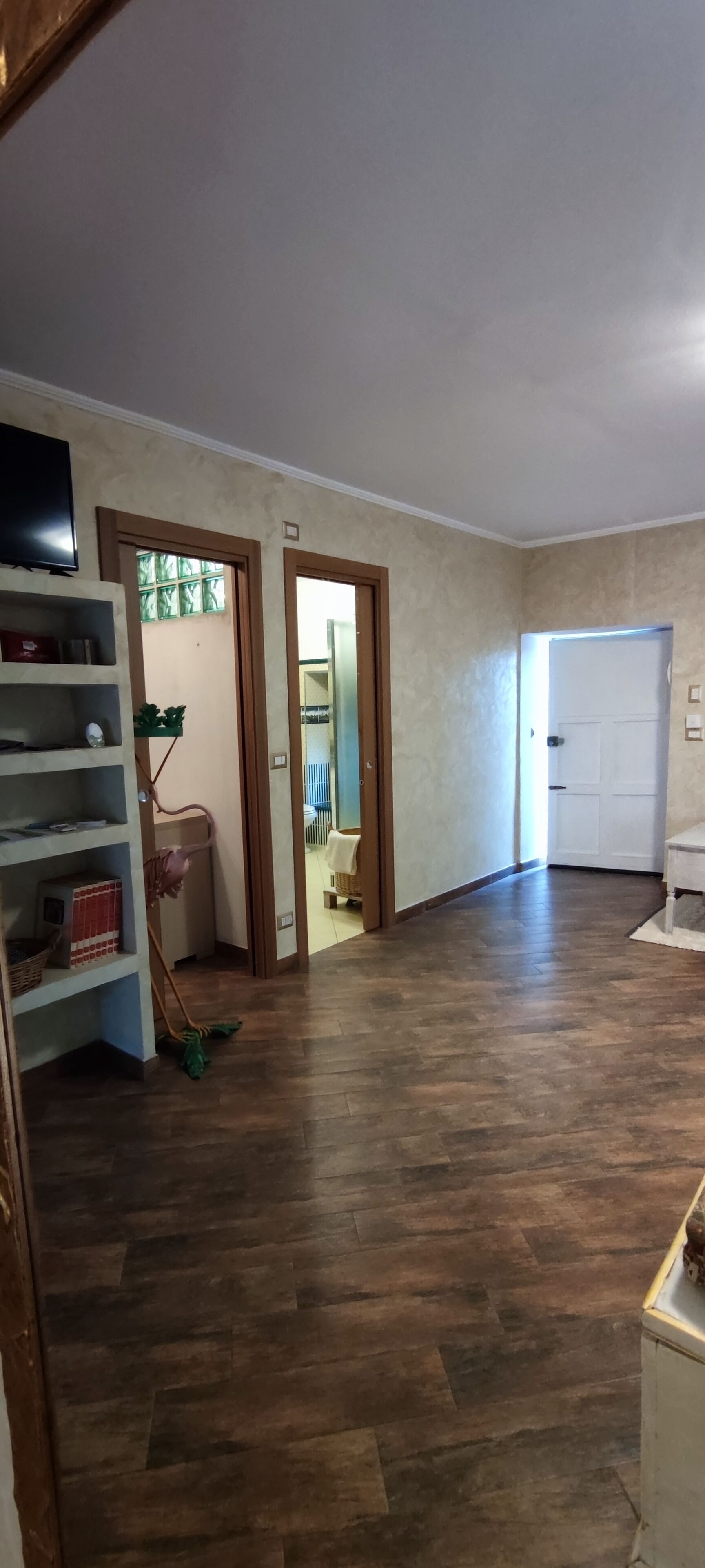 Un'ampia stanza con pavimento in legno, una televisione su uno scaffale e una porta che dà su un'altra stanza.