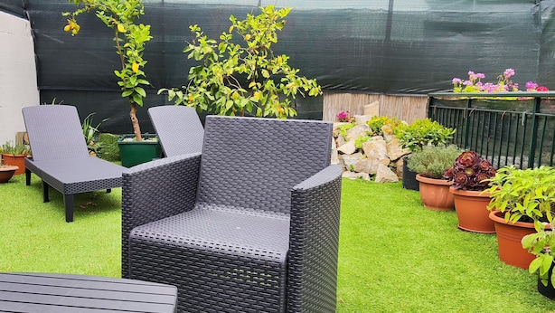 Un espace extérieur aménagé avec des meubles en osier, des plantes en pot et une pelouse verdoyante.